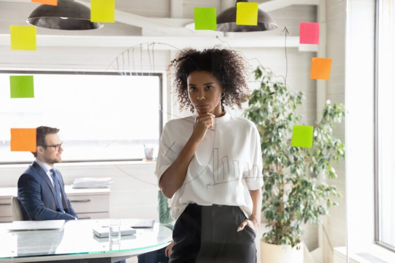 Investor Considers Writing On Glass Wall While Another Sits In The Background.jpg